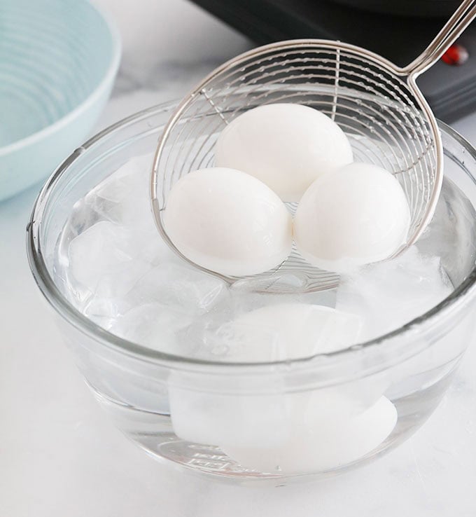 Oeufs durs plongés dans un bol d'eau glacée à l'aide d'une écumoire.