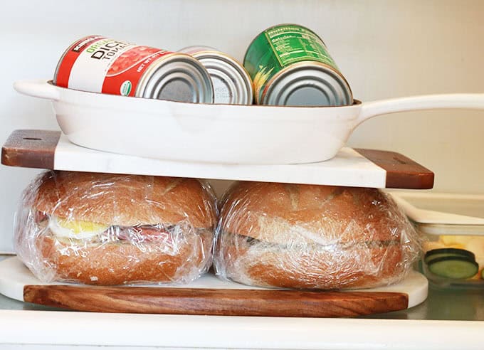 Entre deux plaques, deux sandwichs pan bagnat, presses avec une poêle en fonte et 3 boîtes de conserve.